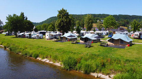 Zicht op tenten en caravans aan de rivier in Campingpark Echternacherbrück, Eifel, Duitsland.
