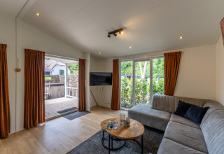 Soggiorno moderno in Family Lodge con divano grigio e vista terrazza a De Thijmse Berg, Paesi Bassi.