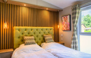 Dormitorio moderno de lodge con dos camas individuales, cabecero verde acolchado, luces y ventana iluminada.