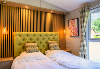 Dormitorio moderno de lodge con dos camas individuales, cabecero verde acolchado, luces y ventana iluminada.