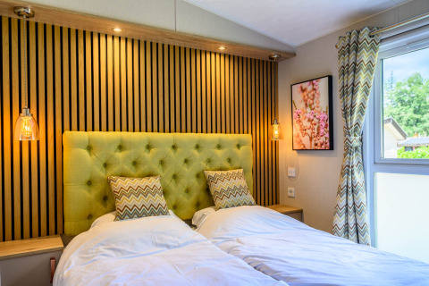 Moderne lodge-slaapkamer met twee eenpersoonsbedden, groene gestoffeerde achterwand, lampen en raam.