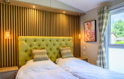 Moderne lodge-slaapkamer met twee eenpersoonsbedden, groene gestoffeerde achterwand, lampen en raam.