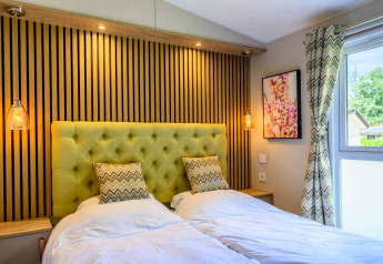 Dormitorio moderno de lodge con dos camas individuales, cabecero verde acolchado, luces y ventana iluminada.