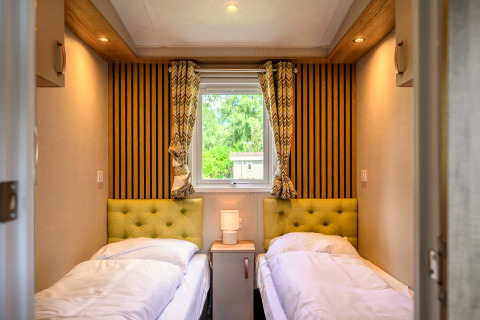 Knusse lodgekamer met twee eenpersoonsbedden, groene hoofdborden, nachtkastje en zicht op buiten.