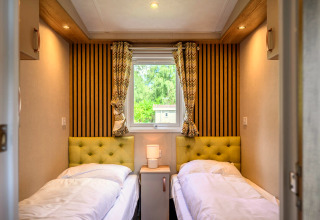 Chambre confortable dans un lodge avec deux lits simples, têtes de lit vertes, table de nuit et fenêtre.