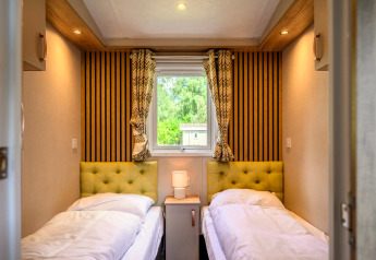 Acogedora habitación de lodge con dos camas individuales, cabeceras verdes, mesita y ventana con vista.