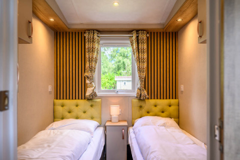 Gezellige lodgekamer met twee eenpersoonsbedden, groene hoofdborden, nachtkastje en raam met uitzicht.