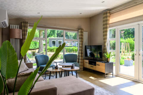 Bright, modern living room in Nova 4 personen lodge at Bospark Ede, Netherlands, with large windows.