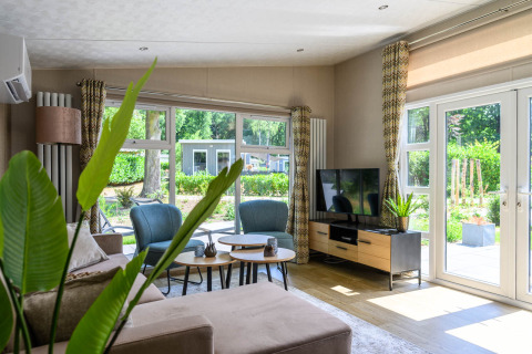 Lyst og moderne stue i Nova 4 personer lodge på Bospark Ede, Nederlandene, med store vinduer og tv.
