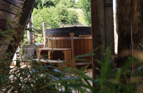 Bañera de hidromasaje exterior en Wellnest, Camping Vinkenhof, Países Bajos, rodeada de naturaleza y árboles.
