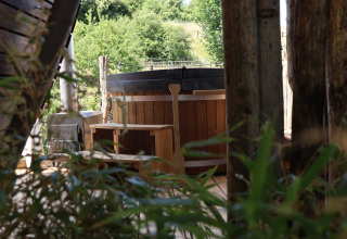 Bañera de hidromasaje exterior en Wellnest, Camping Vinkenhof, Países Bajos, rodeada de naturaleza y árboles.