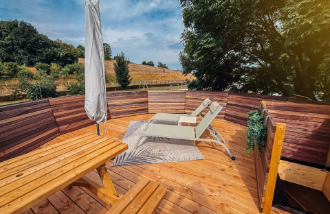Terraza de madera soleada con tumbonas y bancos en Wellnest, Camping Vinkenhof, Países Bajos.