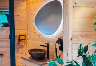 Baño moderno con paneles de madera, lavabo de piedra y espejo singular en Wellnest, Camping Vinkenhof, Países Bajos.