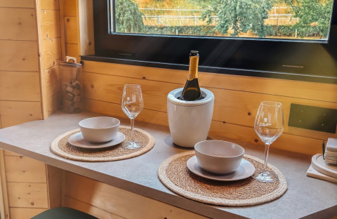 Mesa para dos con vino en Wellnest, Camping Vinkenhof, Países Bajos, junto a una ventana de madera.