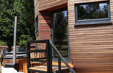 Houten terras en ingang van de Wellnest-lodge bij Camping Vinkenhof in Nederland, tussen de bomen.