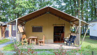 Safari tent at Camping Fuussekaul with covered porch, wooden benches, and chairs set in a leafy area.