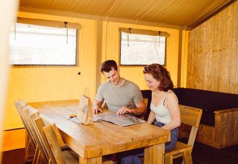 Twee mensen zitten aan een houten tafel in een safaritent op Camping Liefrange in Luxemburg en lezen samen.