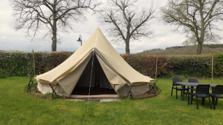 Tipi-telt på Camping Liefrange med åbning foran, græsplæne, bord og stole samt træer i baggrunden.