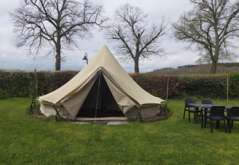 Tenda tipi al Camping Liefrange con ingresso aperto, prato, tavolo, sedie e alberi sullo sfondo.