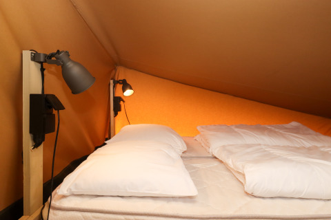 Coin nuit d’une tente safari au Camping Liefrange - Ranger Lodge avec lit double et lampes murales, Luxembourg.