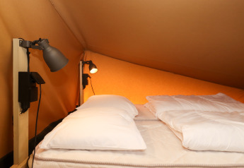 Zona notte in tenda safari al Camping Liefrange - Ranger Lodge con letto matrimoniale e lampade, Lussemburgo.