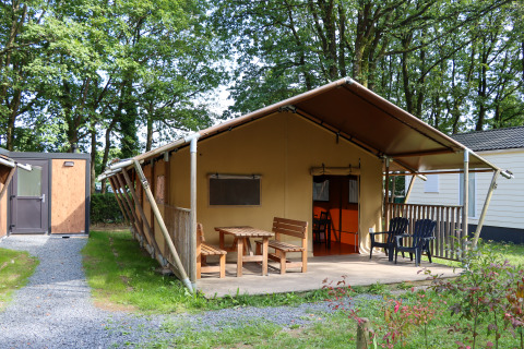 Tente safari avec terrasse et mobilier en bois au Camping Fuussekaul, entourée d’arbres au Luxembourg.