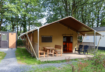 Safari tent with wooden terrace and seating at Camping Fuussekaul, surrounded by trees in Luxembourg.