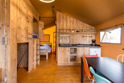 Interno di una tenda safari al Camping Fuussekaul in Lussemburgo con cucina, tavolo e letti visibili.