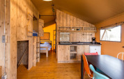 Intérieur d'une tente safari au Camping Fuussekaul au Luxembourg, avec cuisine, coin repas et lits.
