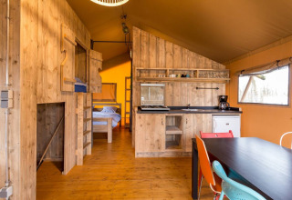Interno di una tenda safari al Camping Fuussekaul in Lussemburgo con cucina, tavolo e letti visibili.