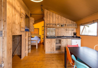 Interior of a cozy safari tent at Camping Fuussekaul in Luxembourg with kitchen, dining, and beds visible.