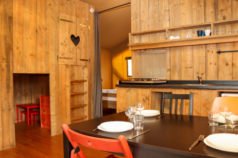 Interior view of Camping Fuussekaul safari tent in Luxembourg, featuring wood walls, kitchen, and dining area.