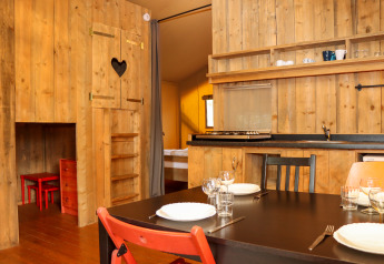 Interior view of Camping Fuussekaul safari tent in Luxembourg, featuring wood walls, kitchen, and dining area.