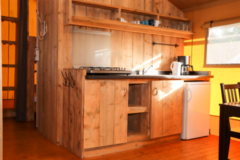 Coin cuisine en bois rustique dans une tente safari au Camping Fuussekaul au Luxembourg avec frigo et plaques.