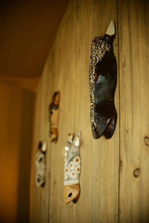 Maschere africane artigianali di animali appese a una parete di legno in una tenda safari al Camping Fuussekaul, Lussemburgo.