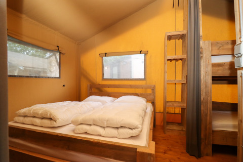 Bedroom in a safari tent at Camping Fuussekaul in Luxembourg with a double bed and bunk beds.