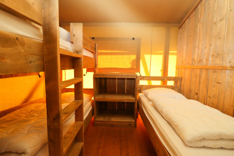 Innenansicht eines Safarizeltes mit Holz-Etagenbetten und Einzelbett im Camping Fuussekaul, Luxemburg.