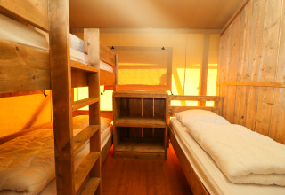 Intérieur d'une tente safari avec lits superposés en bois et lit simple au Camping Fuussekaul au Luxembourg.