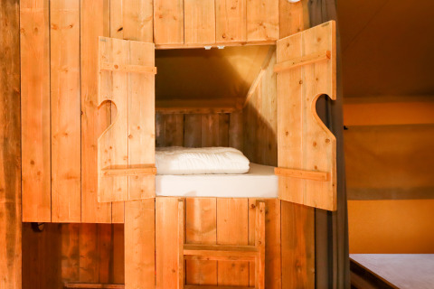 Lit cabine en bois avec portes ouvertes dans une tente safari au Camping Fuussekaul au Luxembourg.