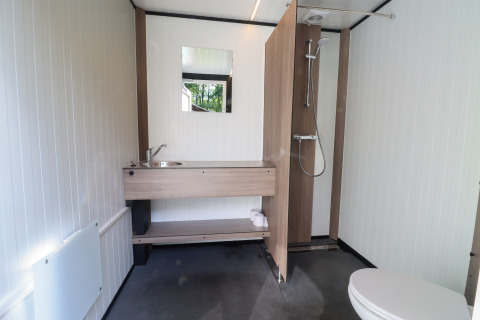 Bagno moderno in una tenda safari, con doccia, lavabo con specchio e wc visibile.