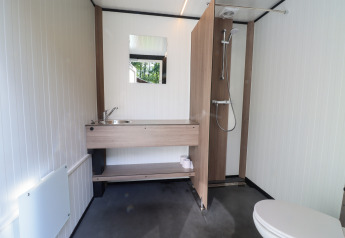 Bagno moderno in una tenda safari, con doccia, lavabo con specchio e wc visibile.
