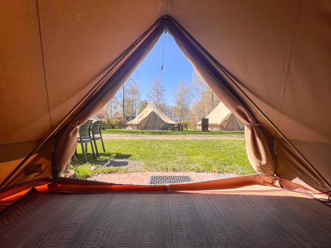 Udsigt fra en tipi-teltåbning på Camping Fuussekaul i Luxembourg, kiggende ud på andre telte og stole.