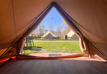 Zicht vanuit een tipi-tent op Camping Fuussekaul in Luxemburg, uitkijkend op grasveld en andere tenten.