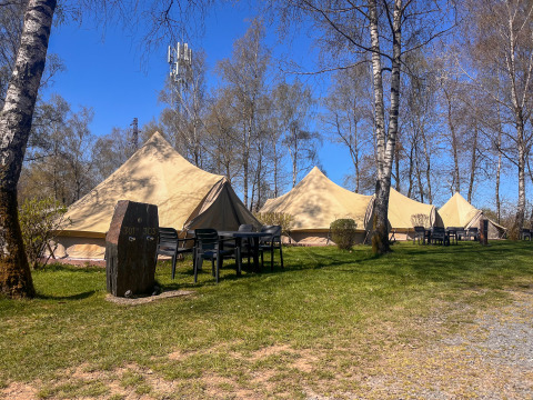 Tipi tents at Camping Fuussekaul in Luxembourg with outdoor seating, trees, and clear blue sky.