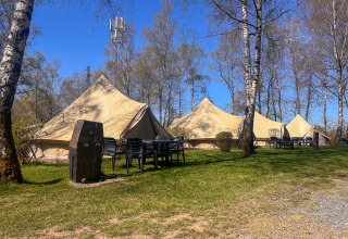 Tende tipì al Camping Fuussekaul in Lussemburgo con tavoli, sedie e alberi sotto un cielo sereno.