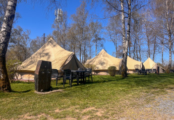Tende tipì al Camping Fuussekaul in Lussemburgo con tavoli, sedie e alberi sotto un cielo sereno.