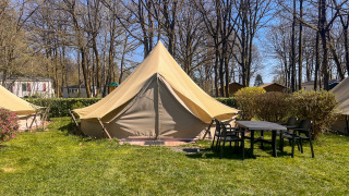 Tipi tent bij Camping Fuussekaul met een tafel en stoelen ervoor, omgeven door gras en bomen.