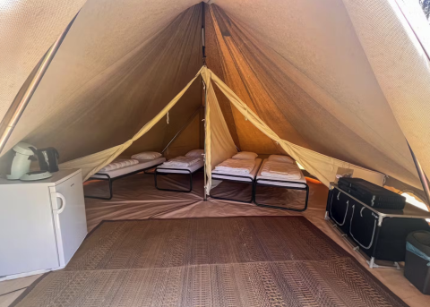 Interno di una tenda tipi con quattro letti, mini frigo e scaffali al Camping Fuussekaul in Lussemburgo.