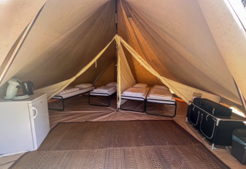 Interno di una tenda tipi con quattro letti, mini frigo e scaffali al Camping Fuussekaul in Lussemburgo.