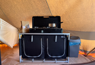Compacte keukenhoek met gasfornuis, pan en prullenbak in een tipi-tent op Camping Fuussekaul, Luxemburg.